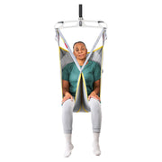 A person seated in a suspended medical or transfer chair with a white frame, gray fabric sling, yellow trim, and black straps, shown against a plain white background.