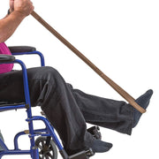 A person using a brown leg extension strap to pull their leg toward a wheelchair, shown against a solid white background.