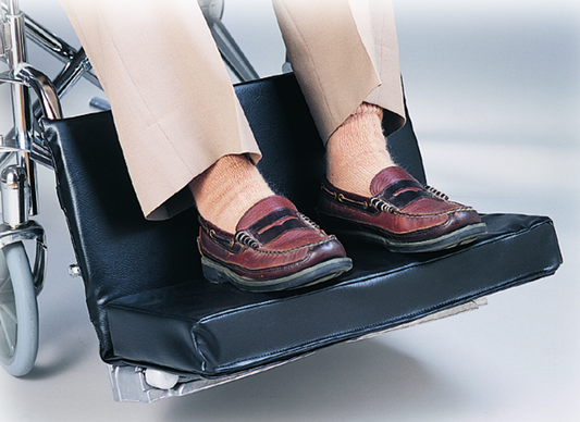 Wheelchair with footrest extended, showing a person's feet wearing brown shoes.