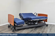 Powered recliner bed with wooden sides and blue mattress in a room setting.
