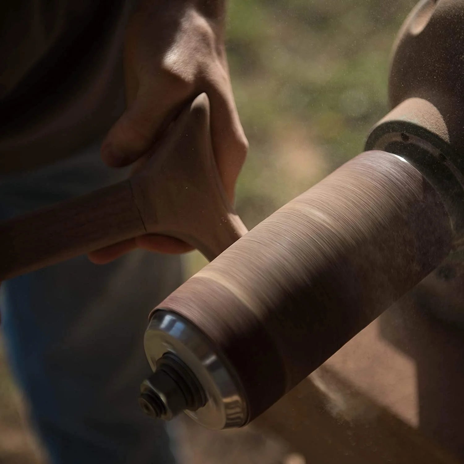 Person holding a wooden spool of thread with a blurred natural background