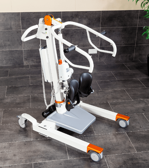 An electric patient transfer lift with a white frame, black seat, and orange accents, shown on a dark tiled floor against a tiled wall.