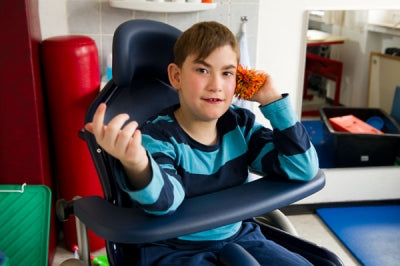 Child sitting in a wheelchair in an indoor setting with colorful equipment around