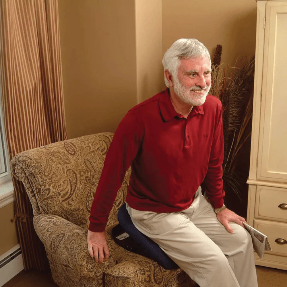 Man sitting on a patterned chair wearing a red shirt and beige pants.