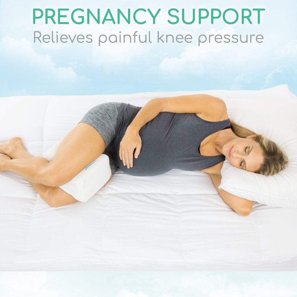Woman lying on a bed using a pregnancy support pillow to relieve painful knee pressure.