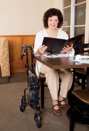 Woman sitting at a table with a folder, next to a walker in a room.