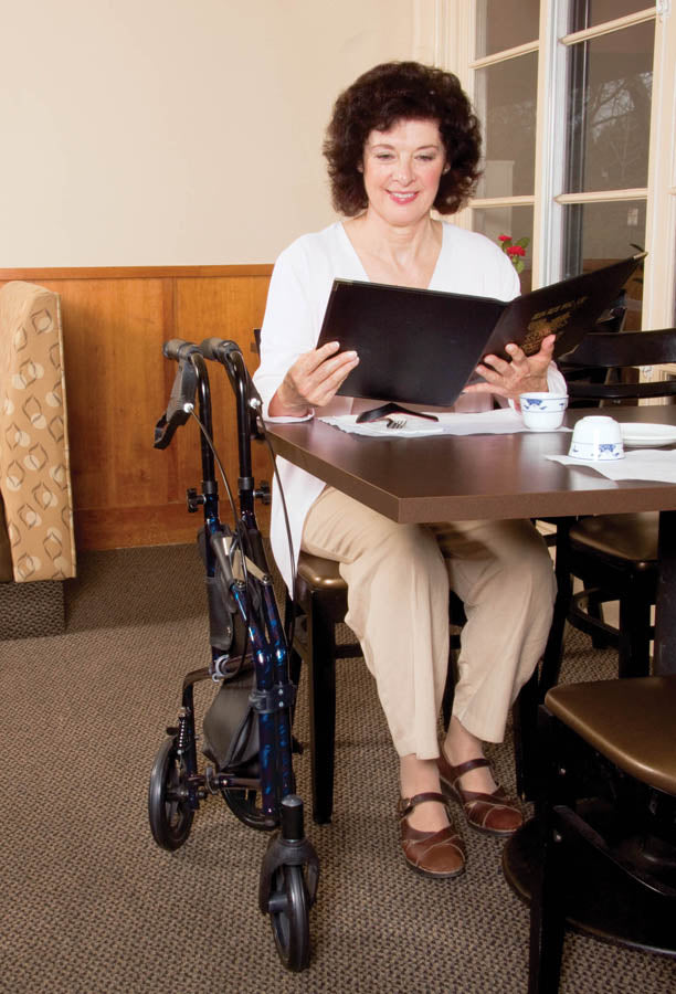 Woman sitting at a table with a folder, next to a walker in a room.