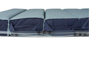 A close-up side view of a padded seat or cushion with a light blue-gray fabric top and a dark navy fabric side panel, resting on a clear plastic base against a white background.