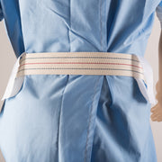A close-up of a light blue scrub or gown with a beige waist belt featuring red and blue dotted stripes, shown on a mannequin or dress form against a plain light background.