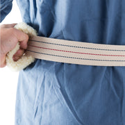A close-up of a person wearing a blue garment, holding a cream-colored woven belt with red and navy stripes and a fluffy cream sherpa loop at one end.