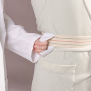 Close-up of a person wearing a textured off-white kimono robe, adjusting the waist sash with a hand pulling the sleeve. The sash is cream with thin red and blue stripes.