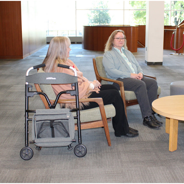 Two women sitting in chairs with a walker and bag in a waiting area.