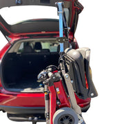 Red mobility scooter with folded chair attached to a car's open trunk.