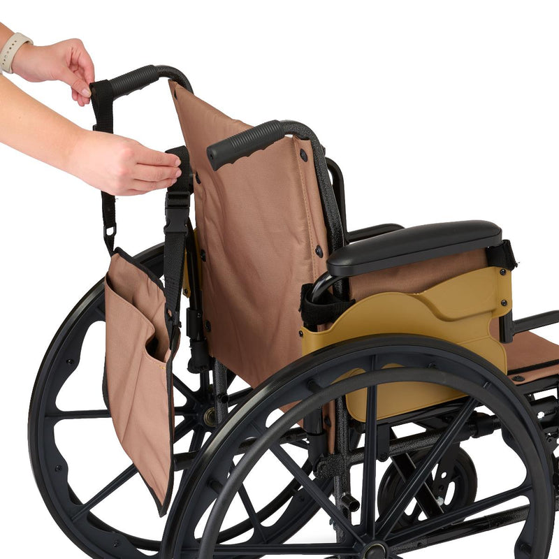 A tan fabric wheelchair accessory, including a backrest cover and side storage pocket, being adjusted onto a black manual wheelchair by a person's hands, shown against a solid white background.