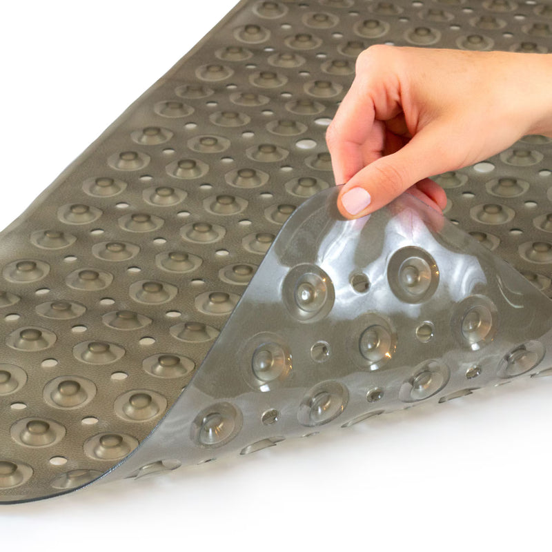 A gray non-slip bath mat with raised circular grips, shown with a hand peeling up one corner to demonstrate its peel-and-stick adhesive backing on a white background.