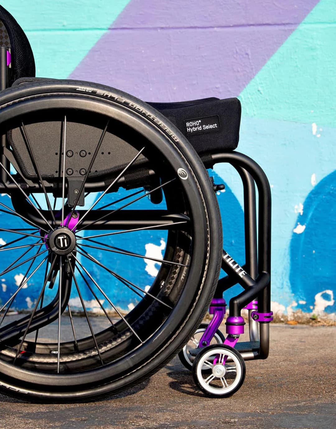 Wheelchair with black and purple accents against a colorful mural background