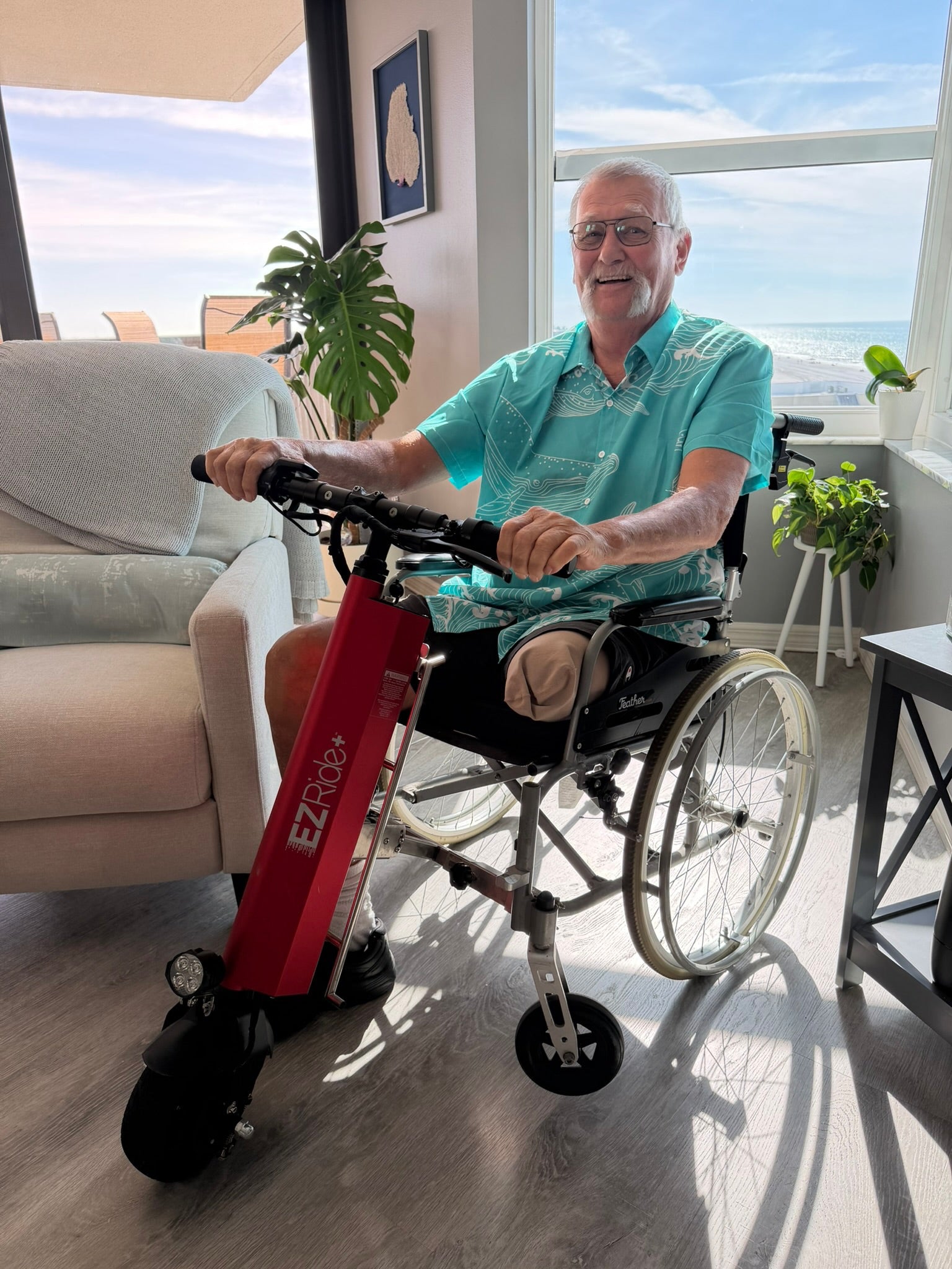 Man using a wheelchair with a red EZ Rider scooter attachment in a sunlit room.