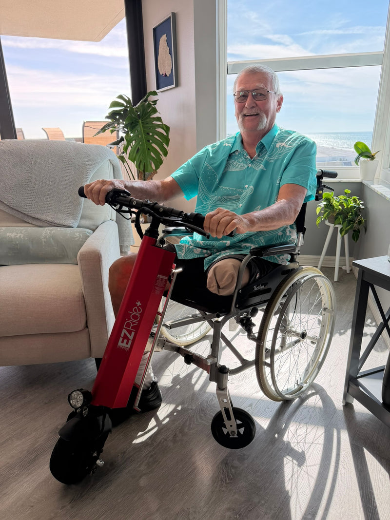 Man using a wheelchair with a red EZ Rider scooter attachment in a sunlit room.