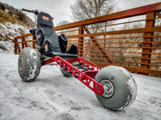 Three-wheeled vehicle with large wheels on a snowy path, wooden fence in the background