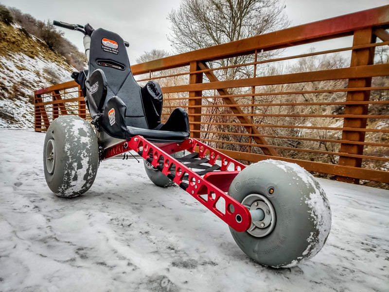 Three-wheeled vehicle with large wheels on a snowy path, wooden fence in the background