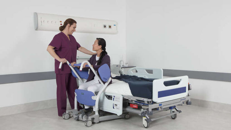 Person being helped onto a hospital bed by a nurse in a clinical setting