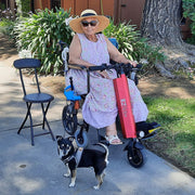 Woman with a dog standing next to an electric scooter on a sidewalk.