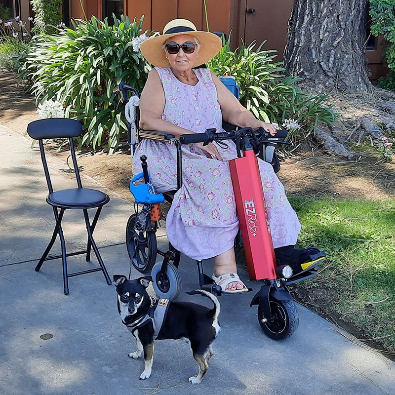 Woman with a dog standing next to an electric scooter on a sidewalk.