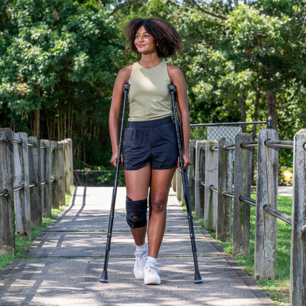 Woman using crutches on a wooden path with greenery in the background