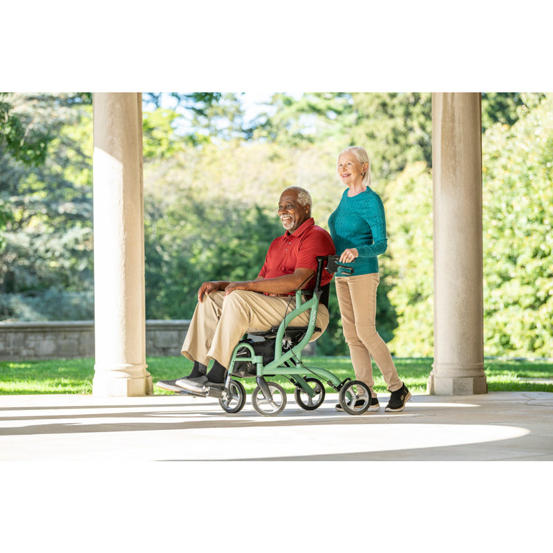 Man in a wheelchair being pushed by a woman outdoors on a sunny day.