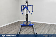 A blue and silver medical lift with a wheeled base stands in a room corner with gray wood-look flooring and light gray walls. The lift is shown with its legs retracted, and text overlays at the bottom read 'Legs Retracted' and 'MED MIZER'.