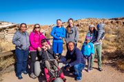 Group of people, including a person in a wheelchair, posing for a photo in a desert landscape.