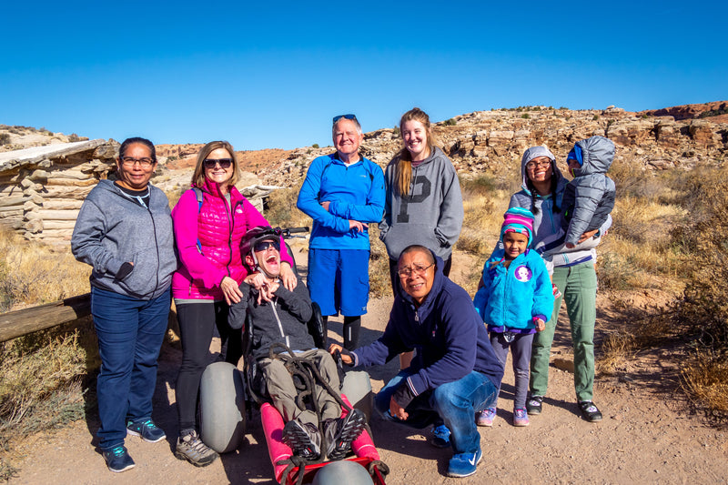 Group of people, including a person in a wheelchair, posing for a photo in a desert landscape.