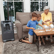 Three people playing a board game in a living room with a home oxygen concentrator.