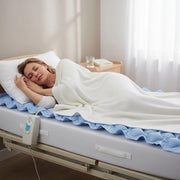 Woman lying in bed with a medical mattress pad in a bright room.