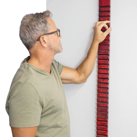 Man holding a red and black striped object against a white wall
