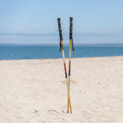 Two hiking poles standing on a sandy beach with ocean and clear sky in the background.