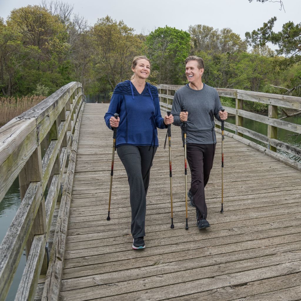 Two people nordic walking on a wooden bridge with trees and water in the background