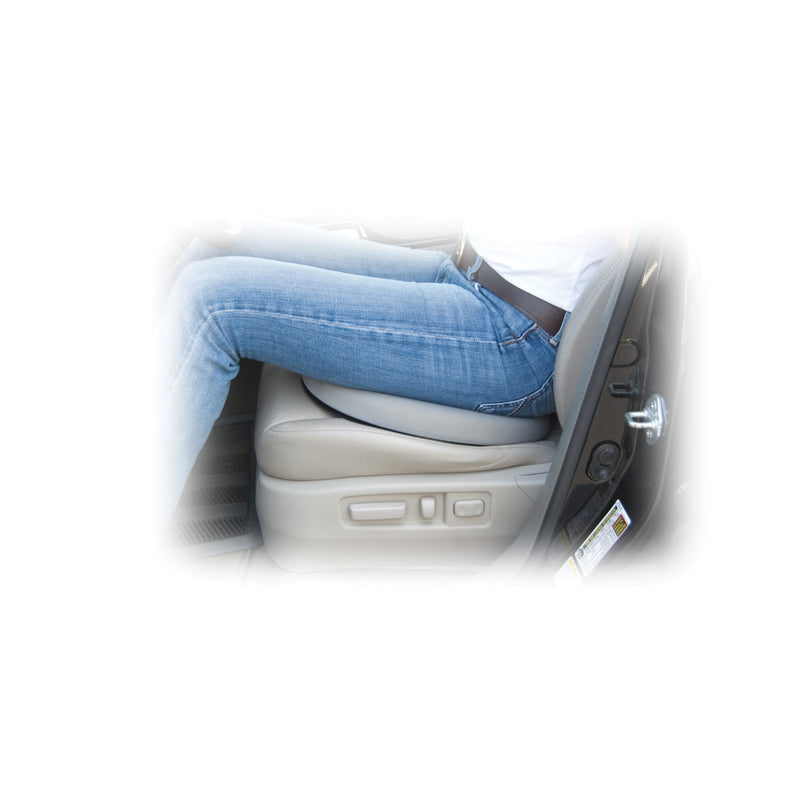 A person wearing blue jeans sits with their legs bent over a beige car seat cushion, shown inside a vehicle. The photo is heavily blurred and low-detail, with a bright white background.