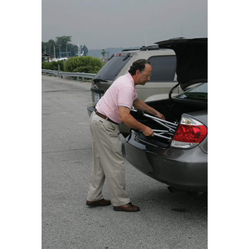 Man loading a suitcase into the trunk of a car in a parking lot.