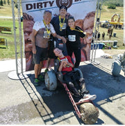 People posing with a decorated cart at an outdoor event, with a 'DIRTY DD' banner in the background.