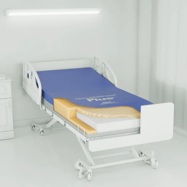 A white hospital-style adjustable bed with a blue mattress and a cutaway view showing yellow and white layers, set in a bright white room.