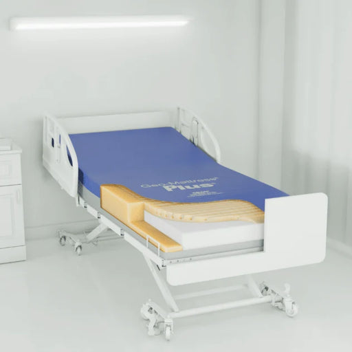 A white hospital-style adjustable bed with a blue mattress and a cutaway view showing yellow and white layers, set in a bright white room.