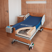 Hospital bed with blue mattress cover in a room with wooden floor and walls.