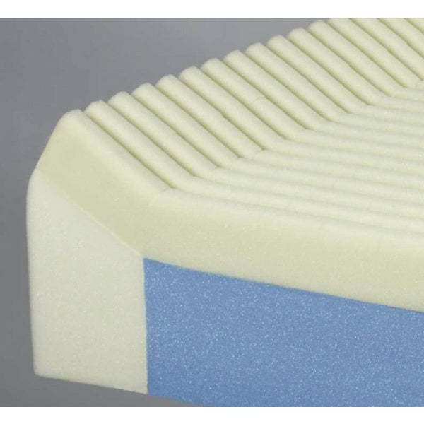 A close-up of a foam mattress topper or cushion showing a cream-colored top section with horizontal grooves and a blue side layer, photographed against a plain gray background.
