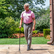 Man walking outdoors with a cane on a wooden deck.
