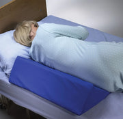 Person lying in bed with a blue wedge pillow under their knees