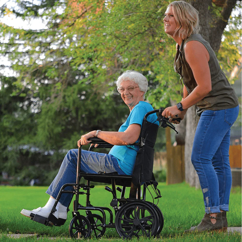 Woman pushing an elderly woman in a wheelchair through a park.