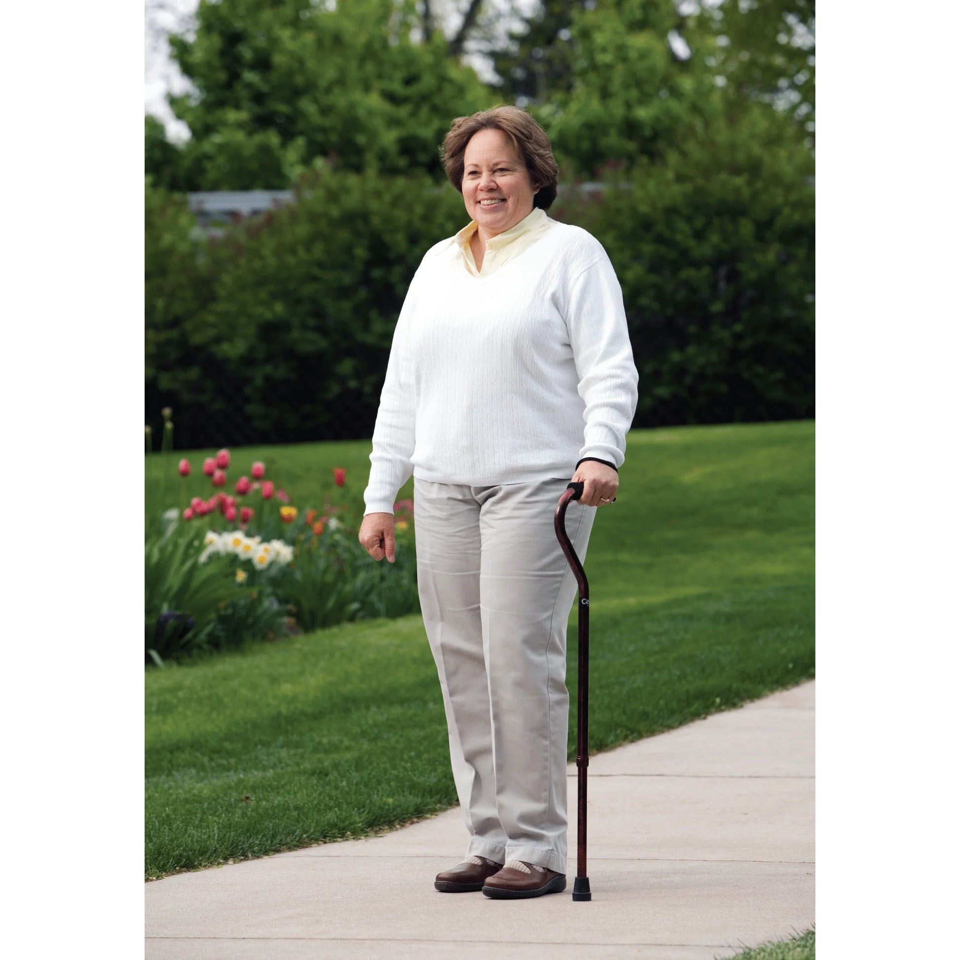 Woman walking outdoors with a cane on a sidewalk