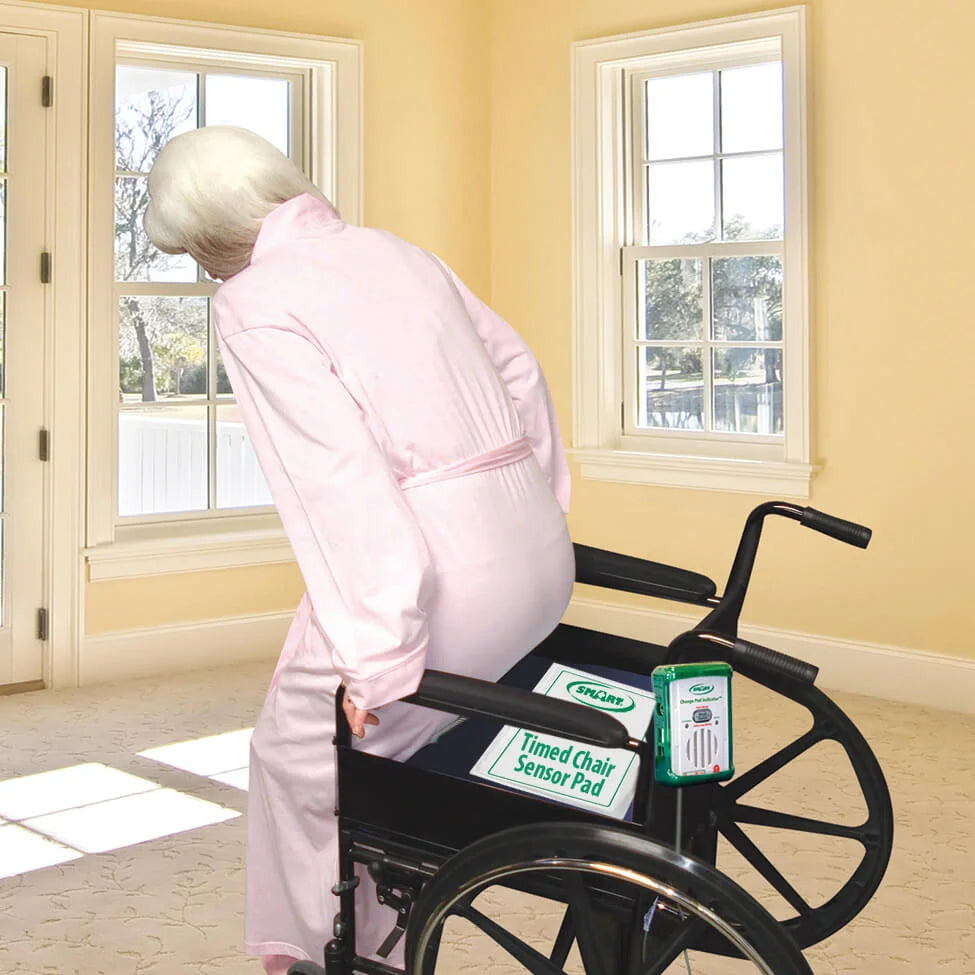 Person in a wheelchair with a timed chair sensor pad attached, in a room with yellow walls and a door.