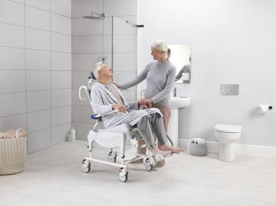 Woman using a shower chair in a bathroom with another person assisting her.